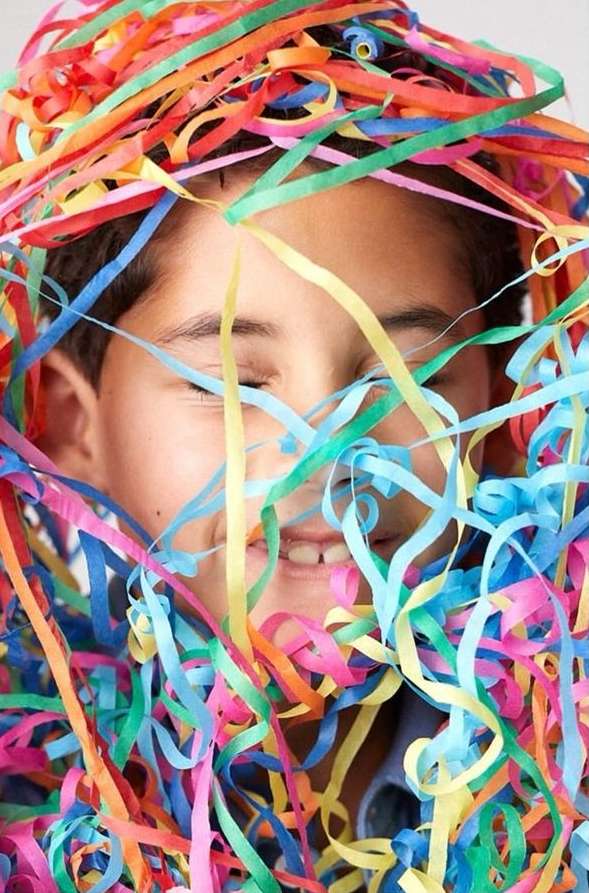 Smiling child surrounded by colorful paper streamers. A fun portrait with bright confetti and a cheerful mood against a light backdrop.