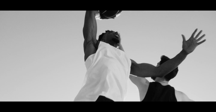 Two men playing basketball outdoors in black and white. One man jumps in the air reaching for the ball.