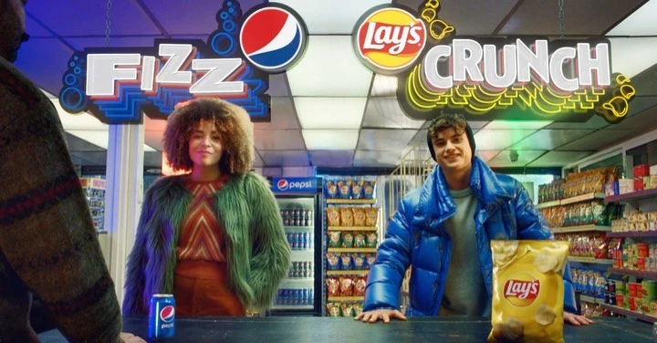Two people standing behind a counter with Pepsi and Lay's branding, creating a vibrant and eye-catching promotional image.