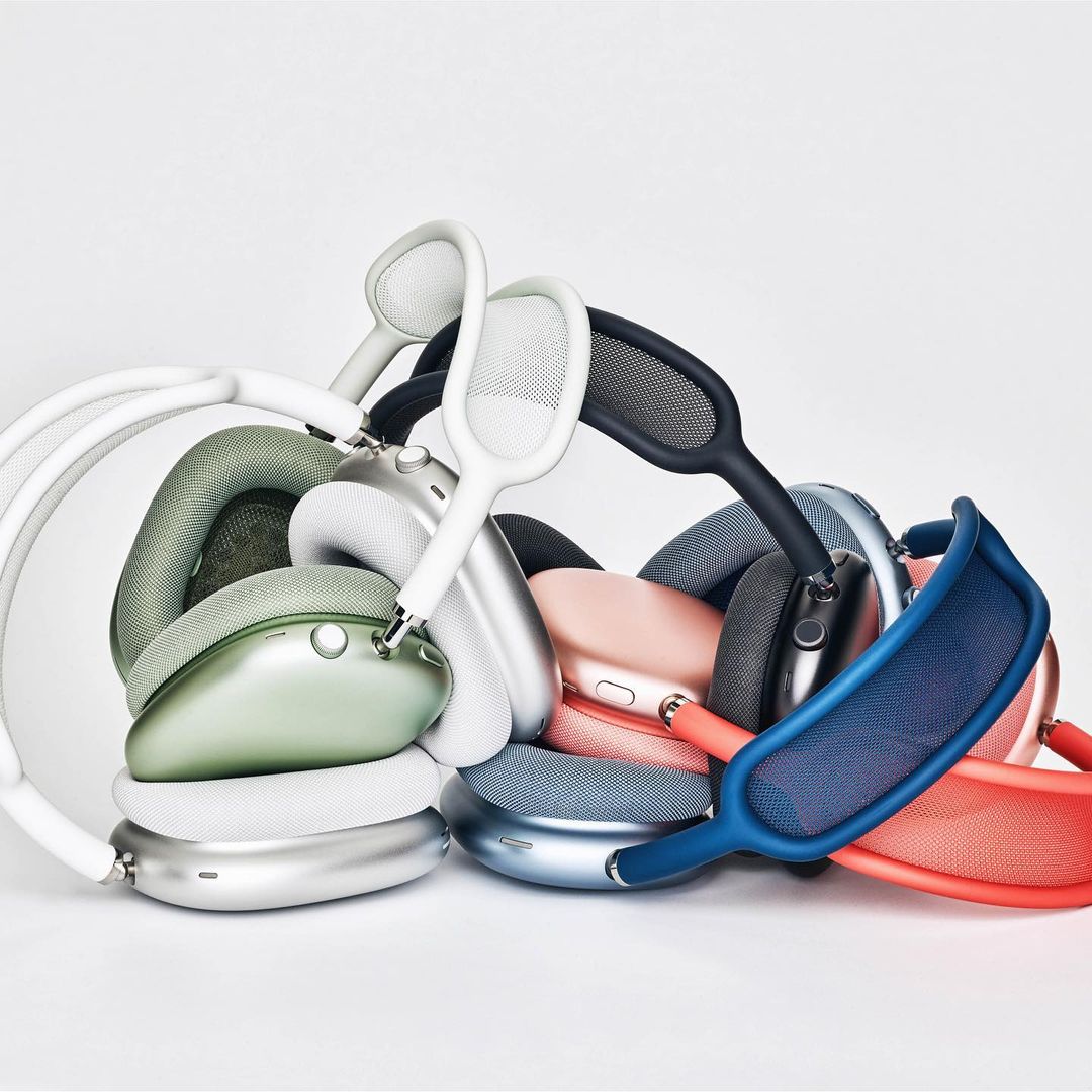 Pile of colorful Apple AirPods Max headphones in white, green, silver, black, pink, blue, and red against a clean white background.