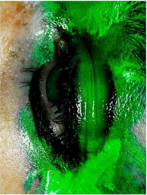 Close-up of an eye with green streaks across the eyelid and around the eye, creating an artistic, vibrant, and slightly surreal effect.