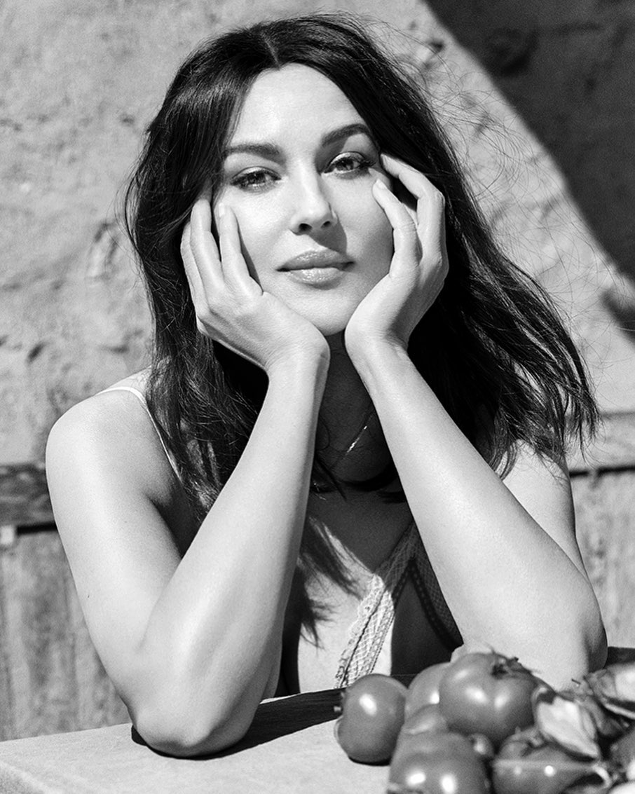 Black and white portrait of Monica Bellucci resting her chin on her hands, tomatoes in the foreground, natural light.