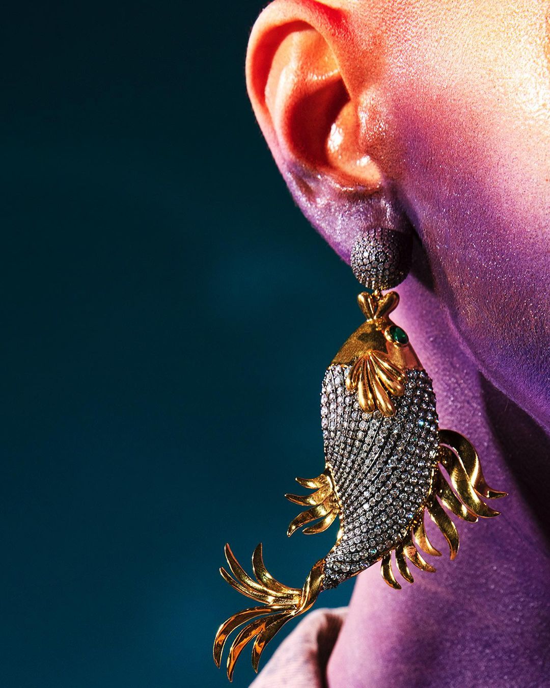Close-up of an earring with gold and silver fish design on a person with iridescent coloring, set against a blue background.