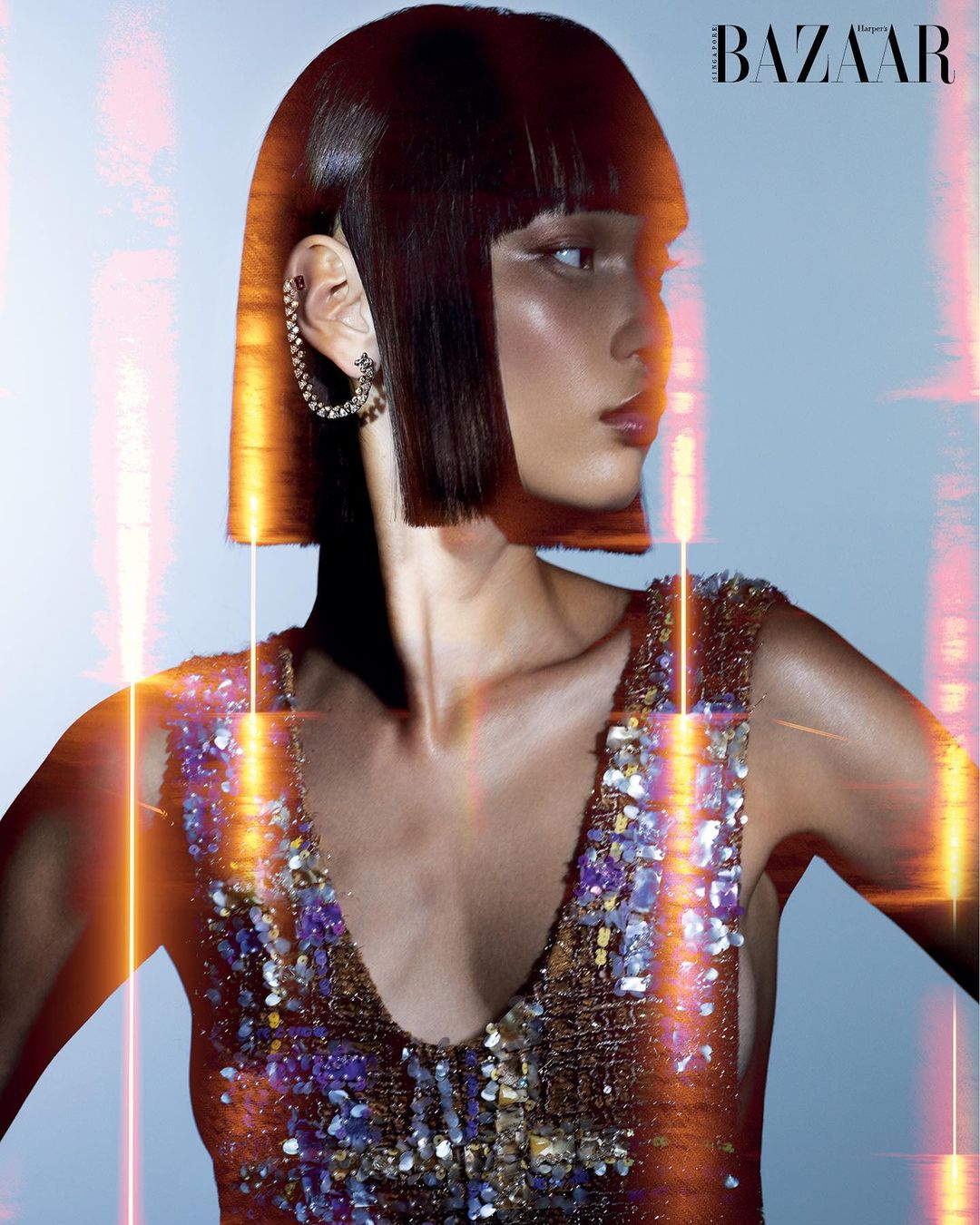 Close-up of a woman with a bob haircut and a sequined dress. She is wearing a silver earring. There is some light flare.