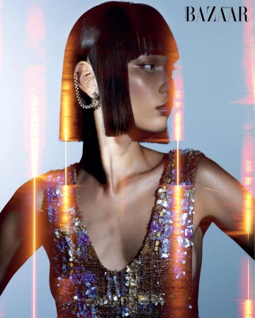 Close-up of a woman with a bob haircut and a sequined dress. She is wearing a silver earring. There is some light flare.