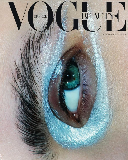 Close-up beauty shot for Vogue Greece magazine cover, featuring a woman's eye with turquoise makeup and dramatic eyebrow, studio lighting.