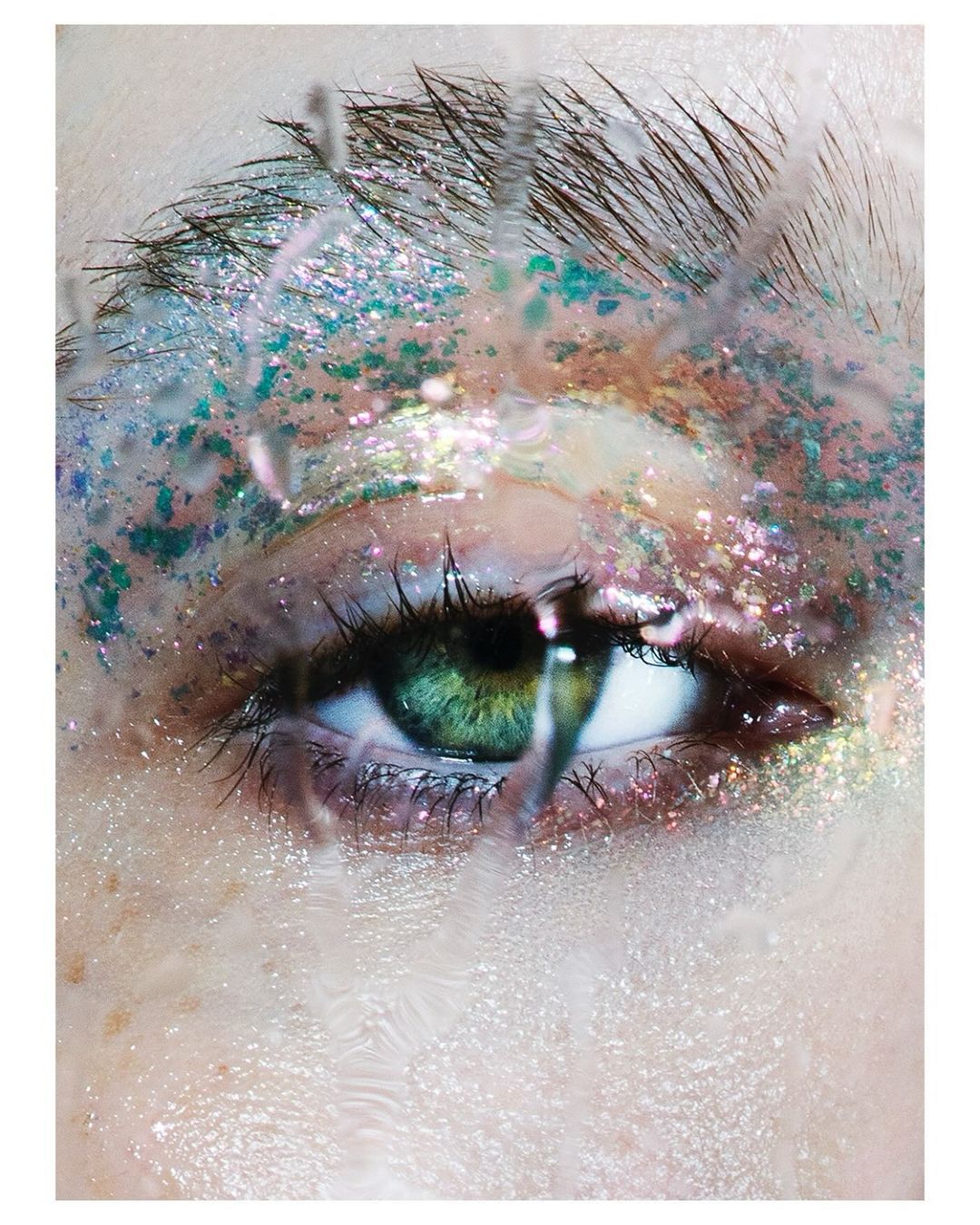 Macro close-up of a person's eye with iridescent makeup and water droplets on the skin, highlighting beauty and intricate detail.