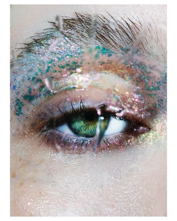 Macro close-up of a person's eye with iridescent makeup and water droplets on the skin, highlighting beauty and intricate detail.