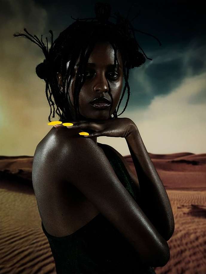 Portrait of a Black woman with striking yellow nails against a desert backdrop, highlighting beauty and fashion elements.