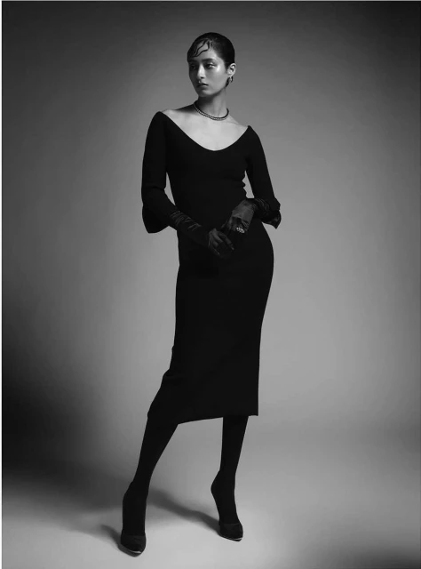Elegant portrait of a woman in a black dress, wearing gloves, set against a neutral backdrop in a studio environment. Fashion photography.