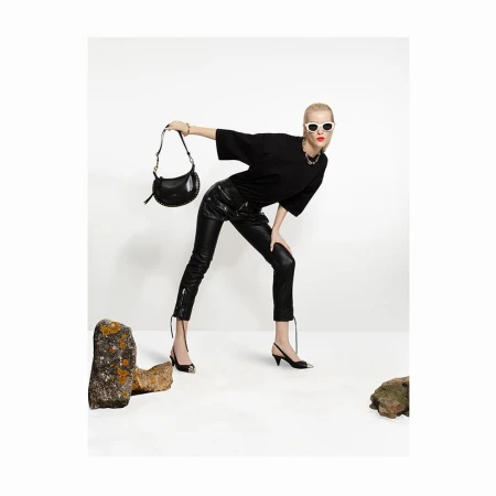 Model in black t-shirt and leather trousers holding a handbag against white studio backdrop with rocks