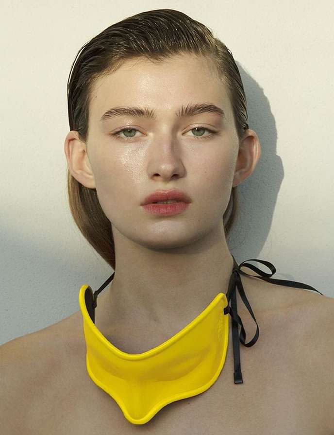 Close-up portrait of a fair-skinned woman wearing a bright yellow collar necklace with black ties, in a beauty and fashion shot.
