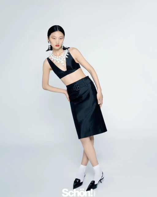 A stylish Asian woman poses indoors wearing a black two-piece outfit, white socks, and black heels against a neutral background.