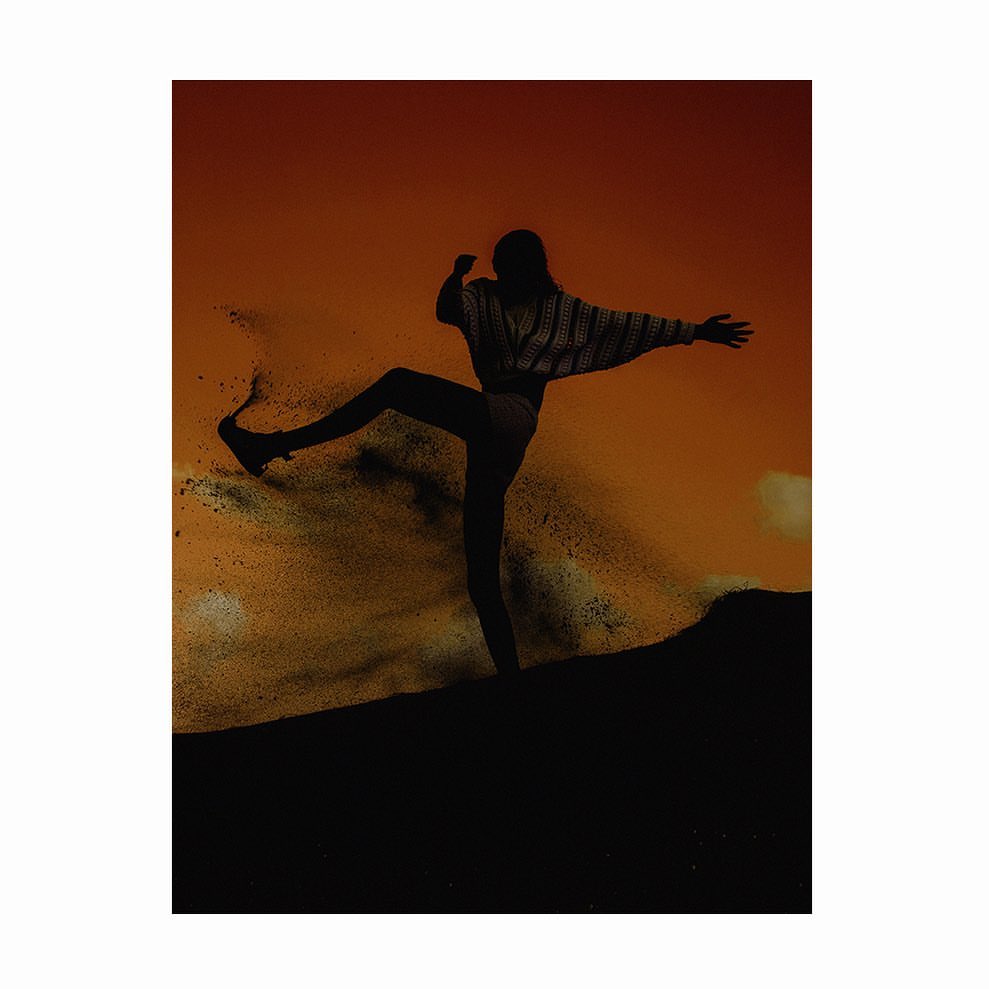 Silhouette of a woman in motion against a warm-toned sky, poised with one leg raised and arms outstretched, creating a dynamic and energetic image.