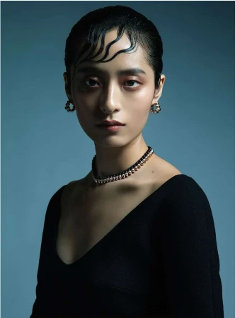Portrait of a woman with wet-styled hair strands on forehead wearing a black top and beaded necklace by Sabine Villiard