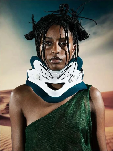 Portrait of a woman wearing a neck brace with an open shoulder dress in front of a desert landscape backdrop, close up studio shot.