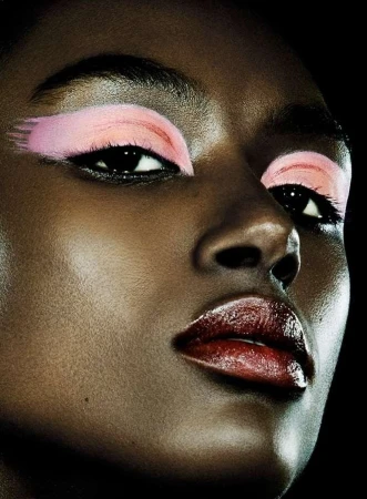 Close-up portrait of a Black woman with bold pink eyeshadow strokes and glossy dark red lips against a black background.