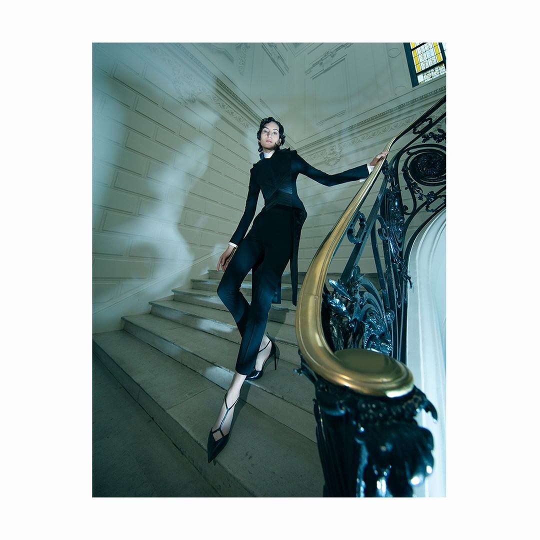 Fashion editorial shot of a female fashion model in a black tailored suit climbing stairs with an ornate gold and black handrail.