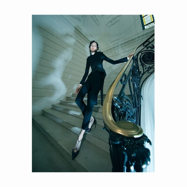 Fashion editorial shot of a female fashion model in a black tailored suit climbing stairs with an ornate gold and black handrail.