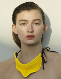 Close-up portrait of a woman with slicked-back hair wearing a yellow statement collar necklace by photographer Sabine Villiard