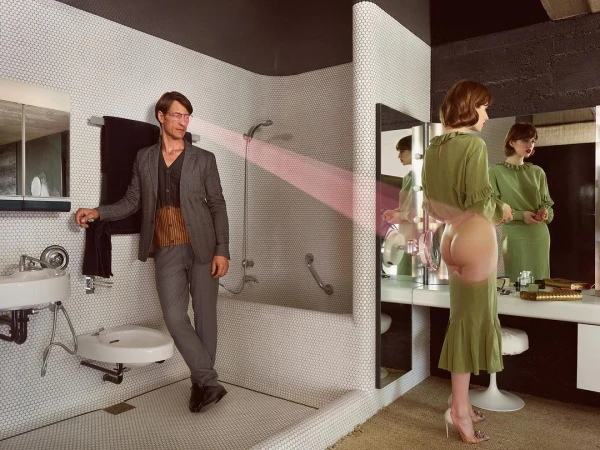 Man leaning against tiled bathroom wall looking at a woman in a green dress standing by a mirror