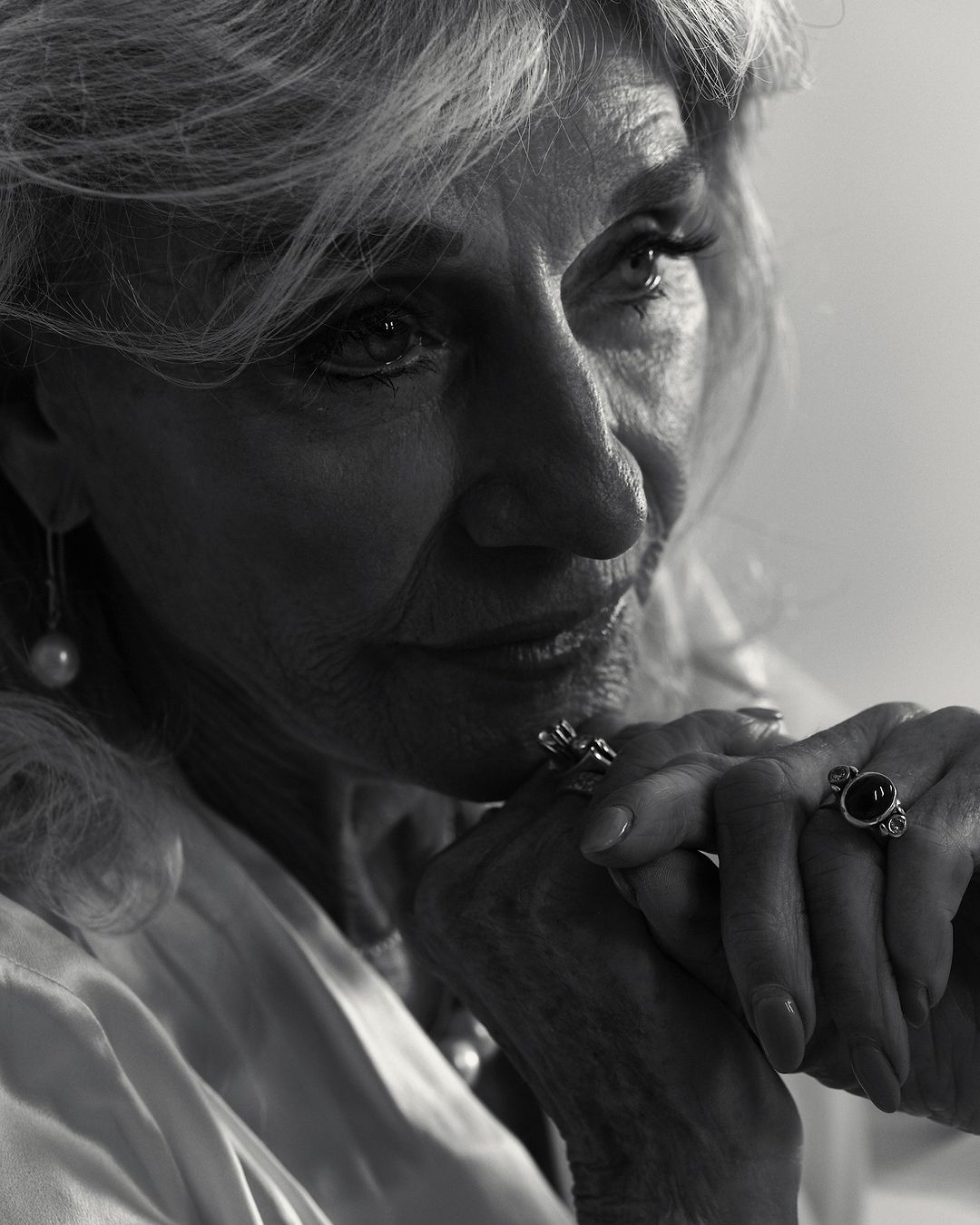 Black and white portrait of an elderly woman with blonde hair wearing jewelry, close-up shot in a brightly lit indoor setting.