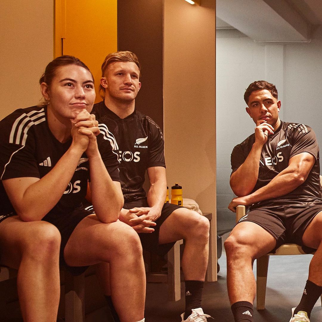 Three athletes in black athletic uniforms seated in an indoor locker room environment photographed by Sacha Stejko.