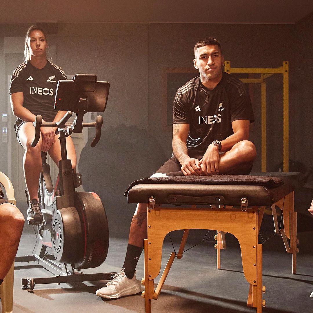 Two athletes, one on an exercise bike and one on a massage table, in a fitness studio, preparing for a workout and recovery.