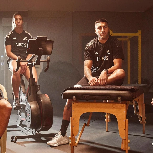 Two athletes, one on an exercise bike and one on a massage table, in a fitness studio, preparing for a workout and recovery.