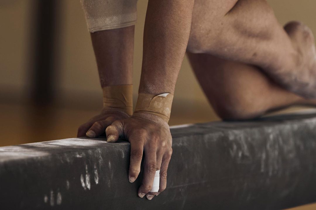 Close-up of gymnast's hands gripping balance beam, wrists taped. Focus on strength, control, and athletic preparation in the sport of gymnastics.