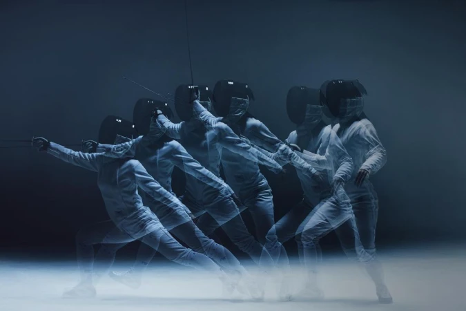 Multiple exposures of a fencer in white fencing gear and black mask performing a fencing move against a dark background.