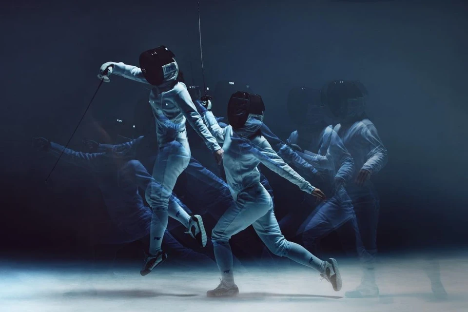 Multiple exposure shot of a person in fencing gear in motion with a sword, wearing a helmet, and clad in protective clothing.