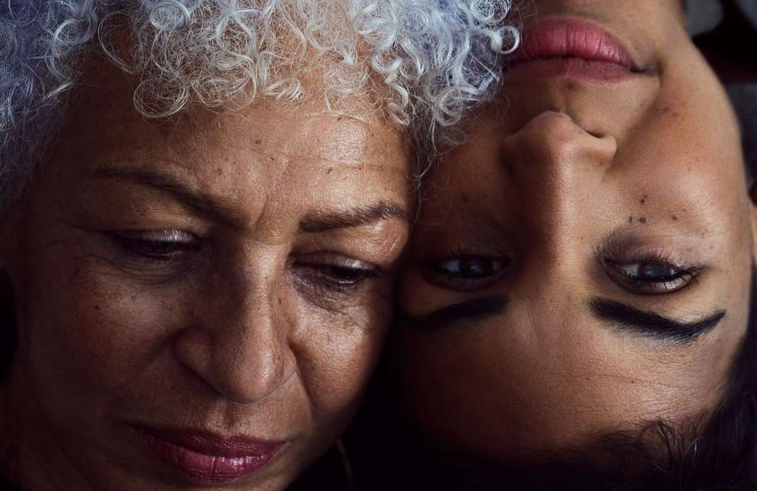 Close-up portrait of an older adult Black woman with grey curly hair and a younger adult Black woman with dark hair, eye contact.