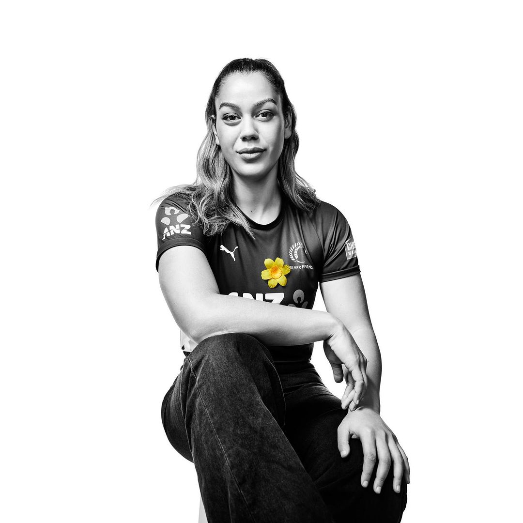 Portrait of an adult woman in sportswear sitting in a photo studio with a white background, her hands resting in her lap.