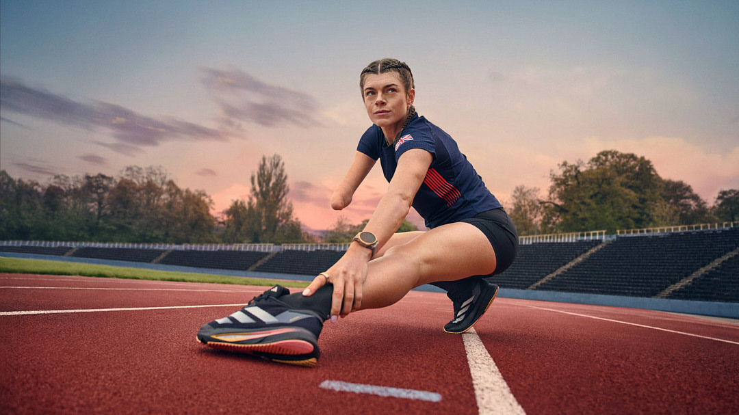 Adaptive athlete stretching her leg on a red running track, wearing a navy blue shirt and black running shorts, outdoor setting.