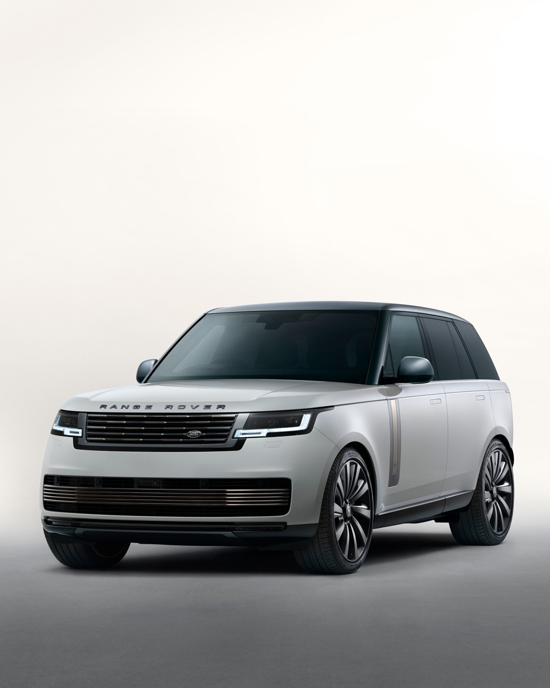 Luxury Range Rover SUV in a studio shot. Car features a light grey exterior, black roof, and large black wheels against soft lighting.