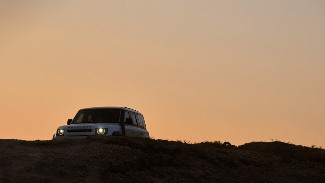Off-road vehicle navigates a silhouetted terrain against a backdrop of orange sky at dusk, showcasing automotive capabilities.