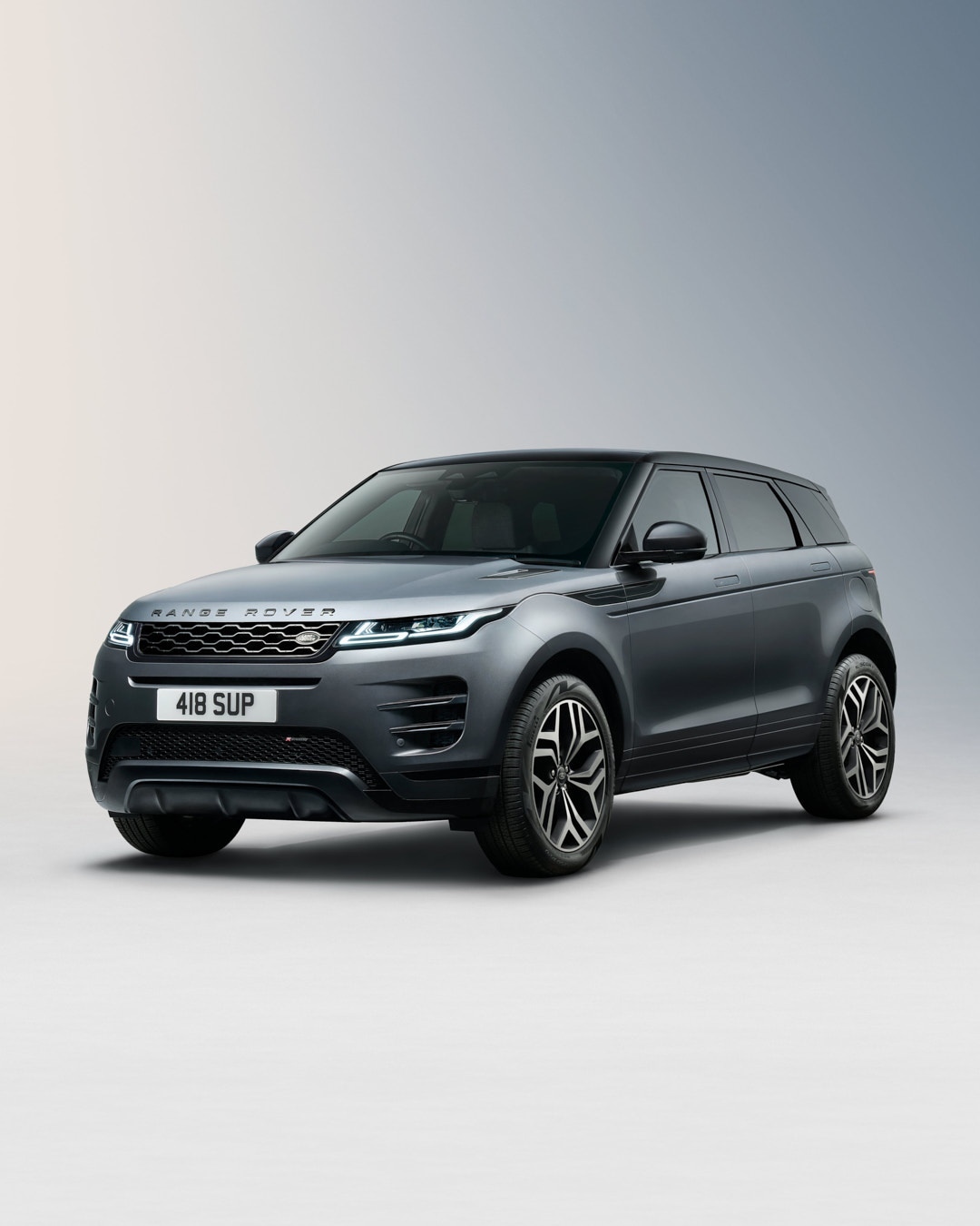 Grey Range Rover Evoque three-quarter studio shot with black wheels and roof, silver grille, and ‘Range Rover’ nameplate on the hood.