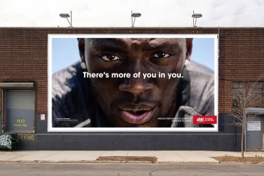 Outdoor billboard advertisement featuring a close-up portrait of a Black man with intense gaze on a brick building exterior.
