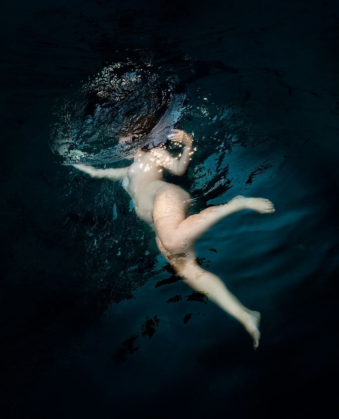 Underwater shot of an adult woman swimming in dark water, showcasing a unique and artistic perspective with bubbles and dynamic movement.