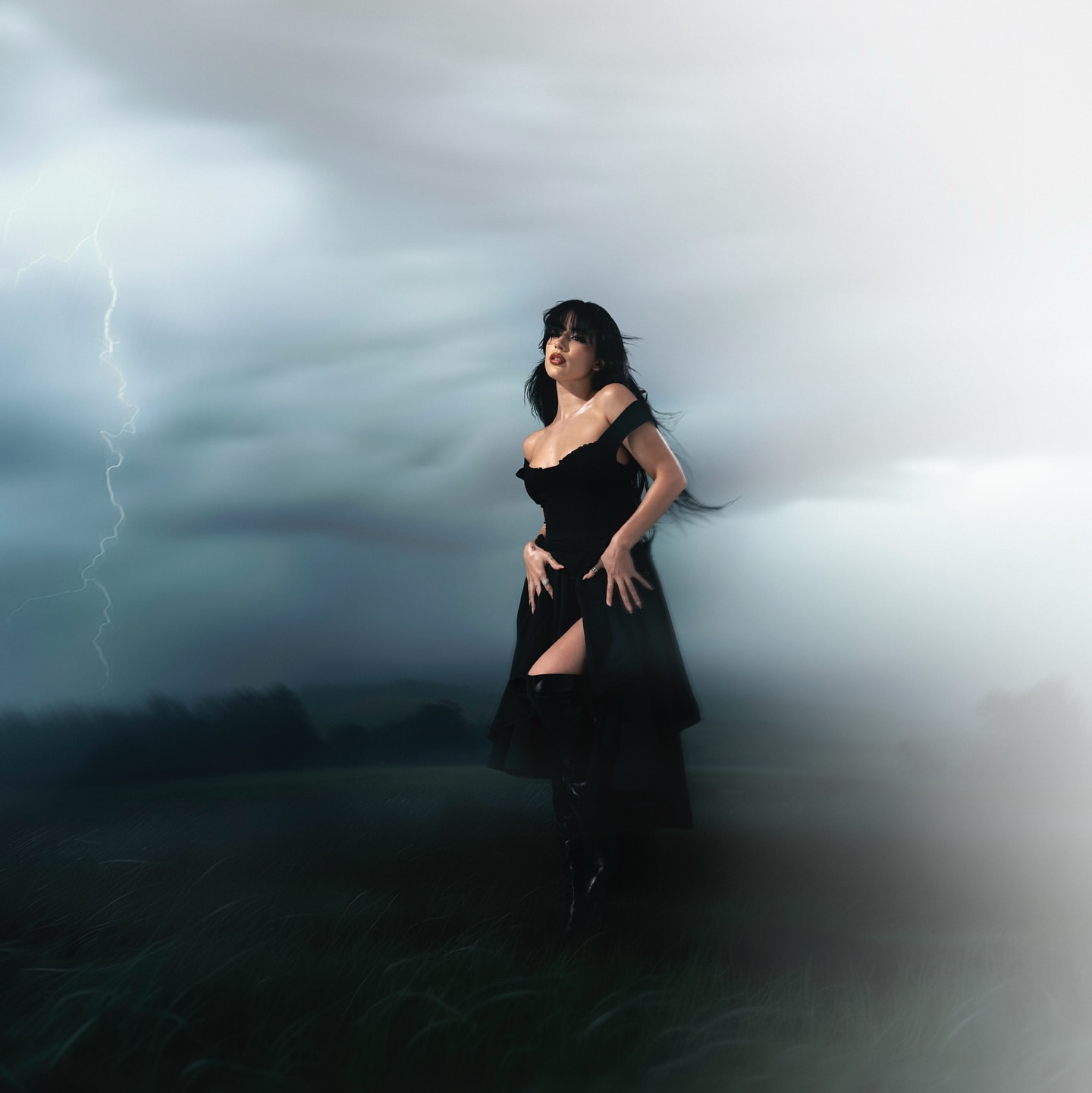 Woman in black dress posing outdoors with lightning in the distance. Dark, moody aesthetic. Atmospheric and dramatic.