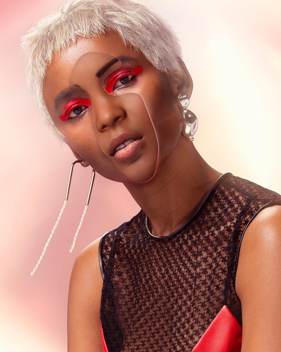 Close-up portrait of a young woman with short hair, red eye makeup, and statement earrings against a soft gradient background.
