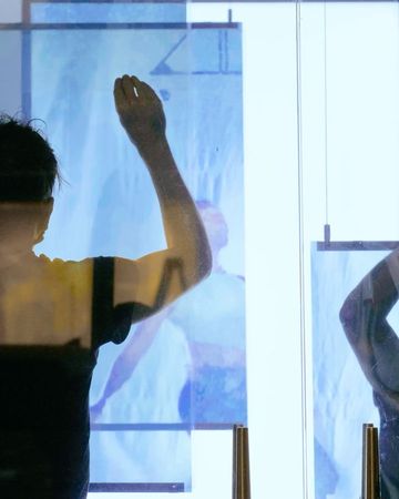 Back view of a person touching a glass panel with an image of a body on it, illuminated by white light.