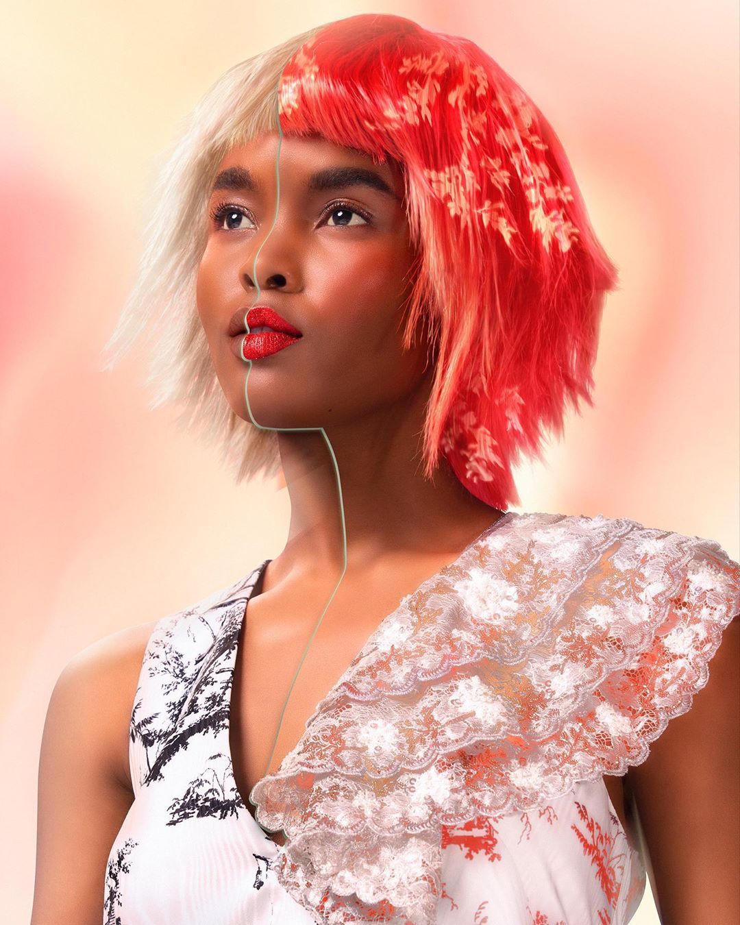 Artistic portrait of a woman with split-dyed red and blonde hair, red lipstick, and a patterned dress, gazing upwards in a studio setting.