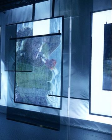 View of an art installation with translucent photo prints suspended by metal frames in an exhibition space, showcasing contemporary artwork.