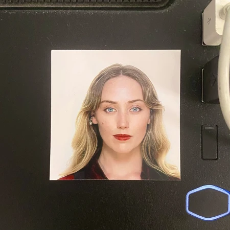 Headshot of a fair-skinned woman with long blonde wavy hair, blue eyes, and red lipstick, wearing a red and black patterned top.