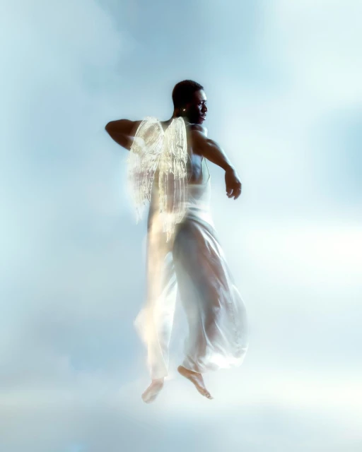African-American man wearing a white outfit with artistic light effects creating faux wings, soft light, against a sky-blue background.