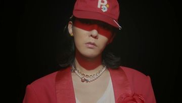 Person in red cap and blazer with pearl necklaces against black background. Fashion portrait.