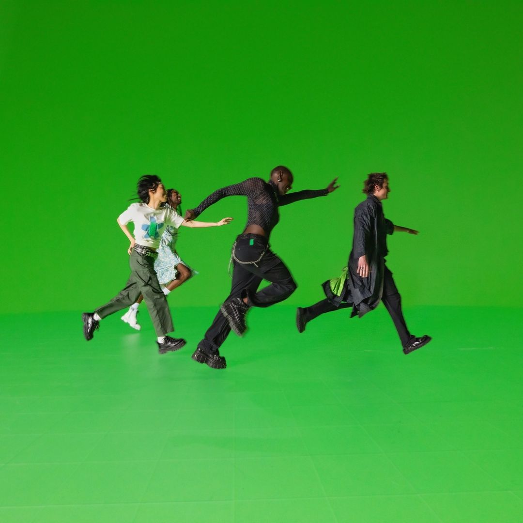 Four people in athletic wear running at eye level against a bright green backdrop, motion blur suggests speed and energy.