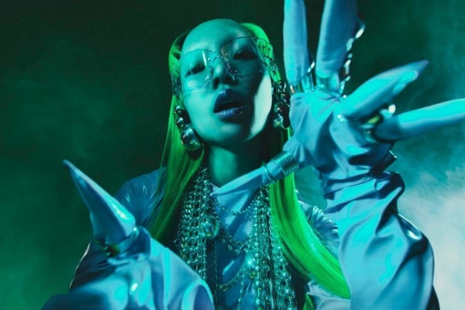 Person with green hair, futuristic glasses, sculptural gloves and jewelry in a studio shot with blue and green lighting and fog.